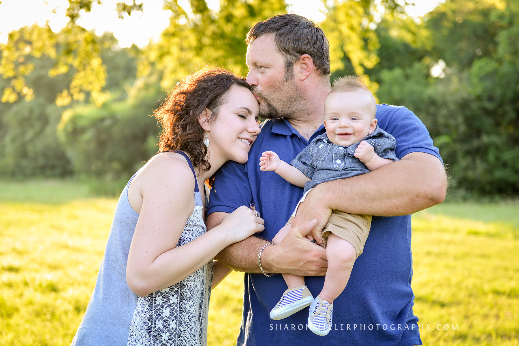 photo of Dad kissing Mom while holding a smiling baby by Lewisville family photographer Sharon Miller