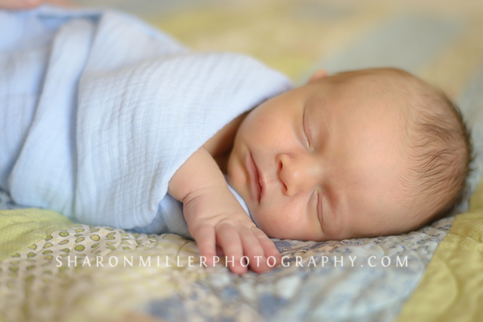photo of a swaddled newborn baby boy sleeping on a blue and green quilt