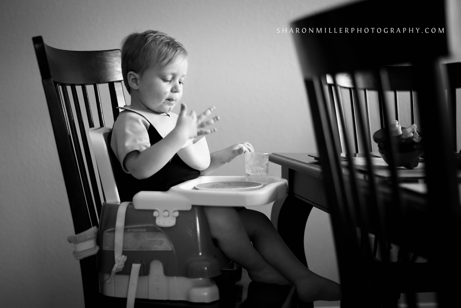 toddler sitting in a booster seat at the dining room table finishing his favorite snack