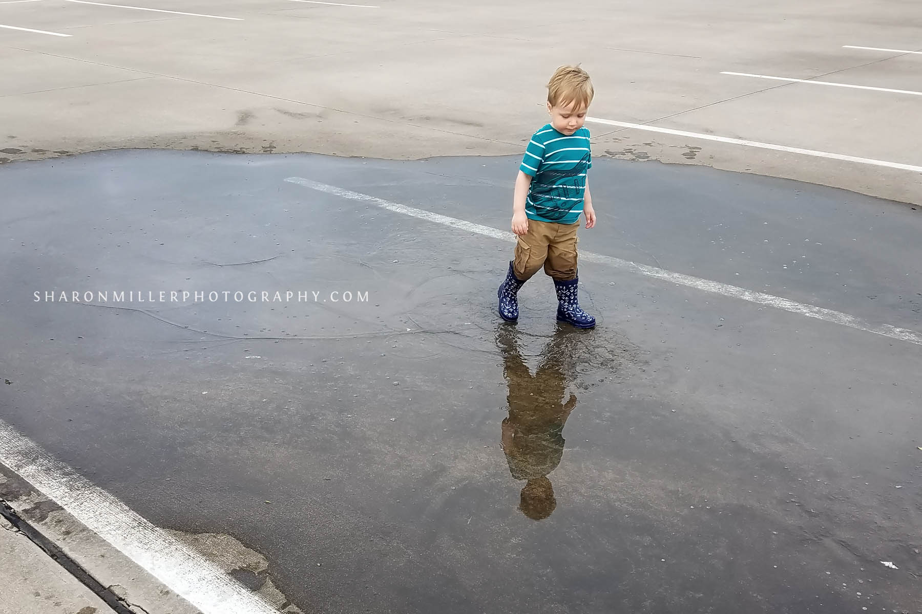 boy wearing rain boots stomping in a puddle in a parking lot