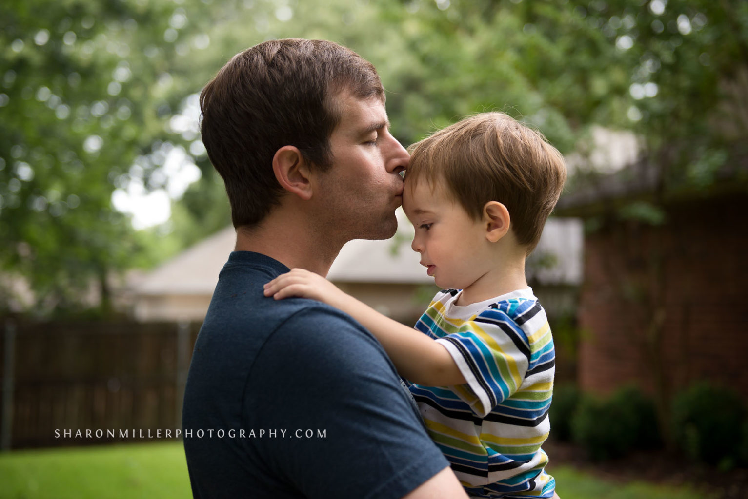 dad holding toddler son kissing him on the forehead
